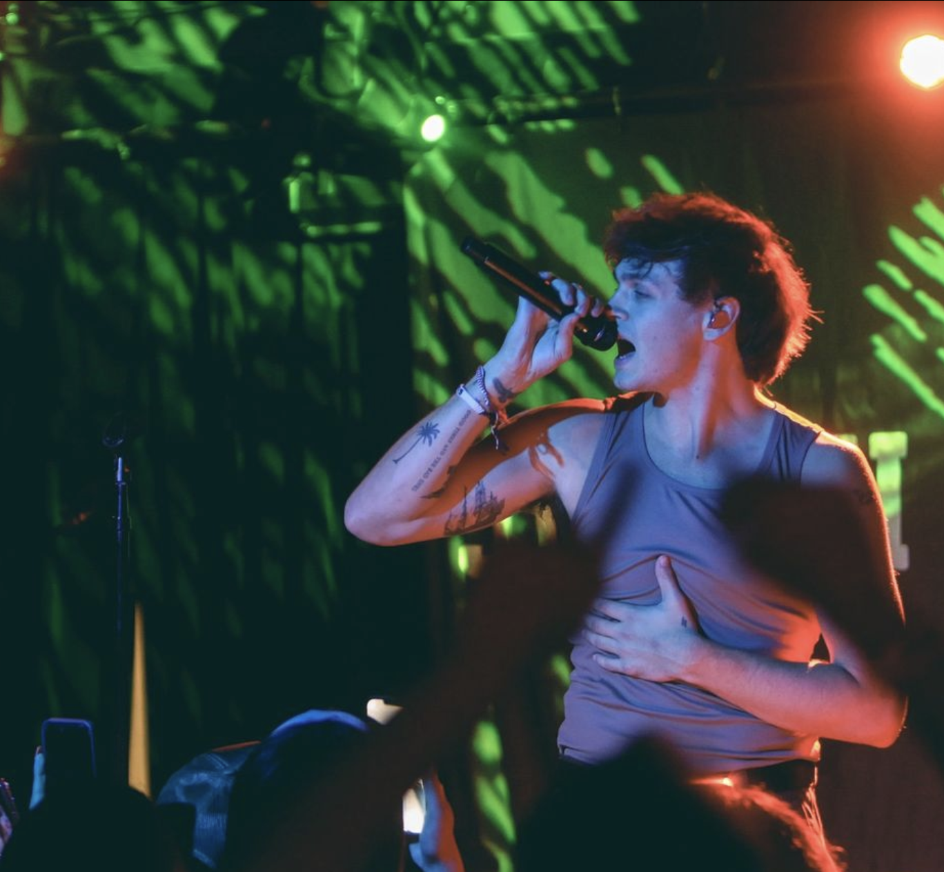 Jonah posing to the left while holding onto the microphone. Their are bright green lights behind him.